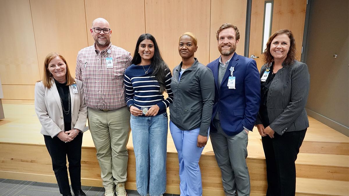 Group of five people from UNC Health's nursing program presenting a student, Neha Varrier, a challenge coin for her efforts in saving a person's life with CPR.